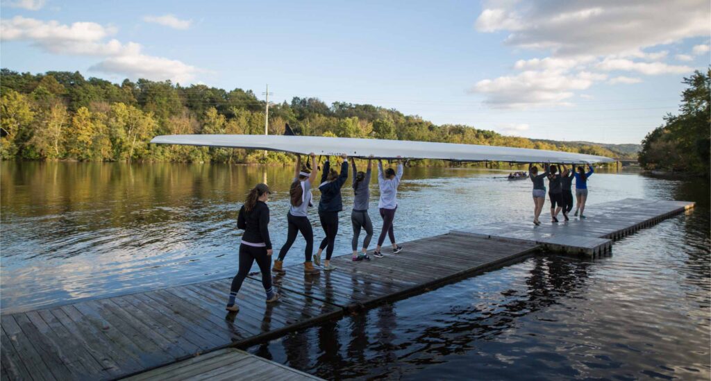 Students are collectively moving a rowing boat on the river floating deck.
