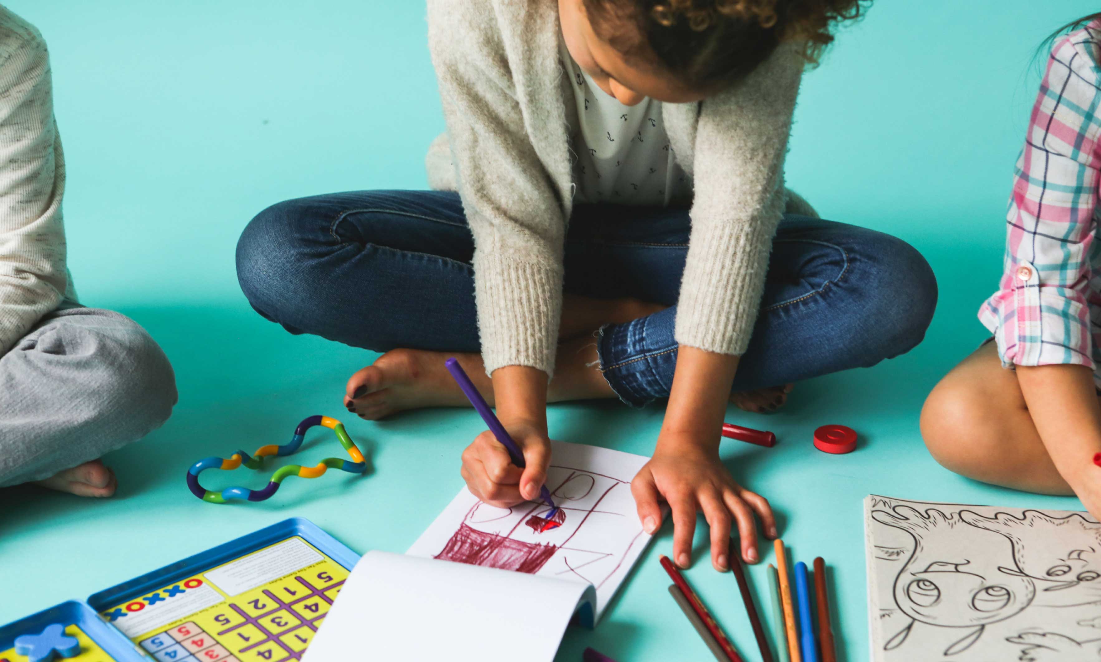 A child is sitting on the floor, drawing in a sketchbook.