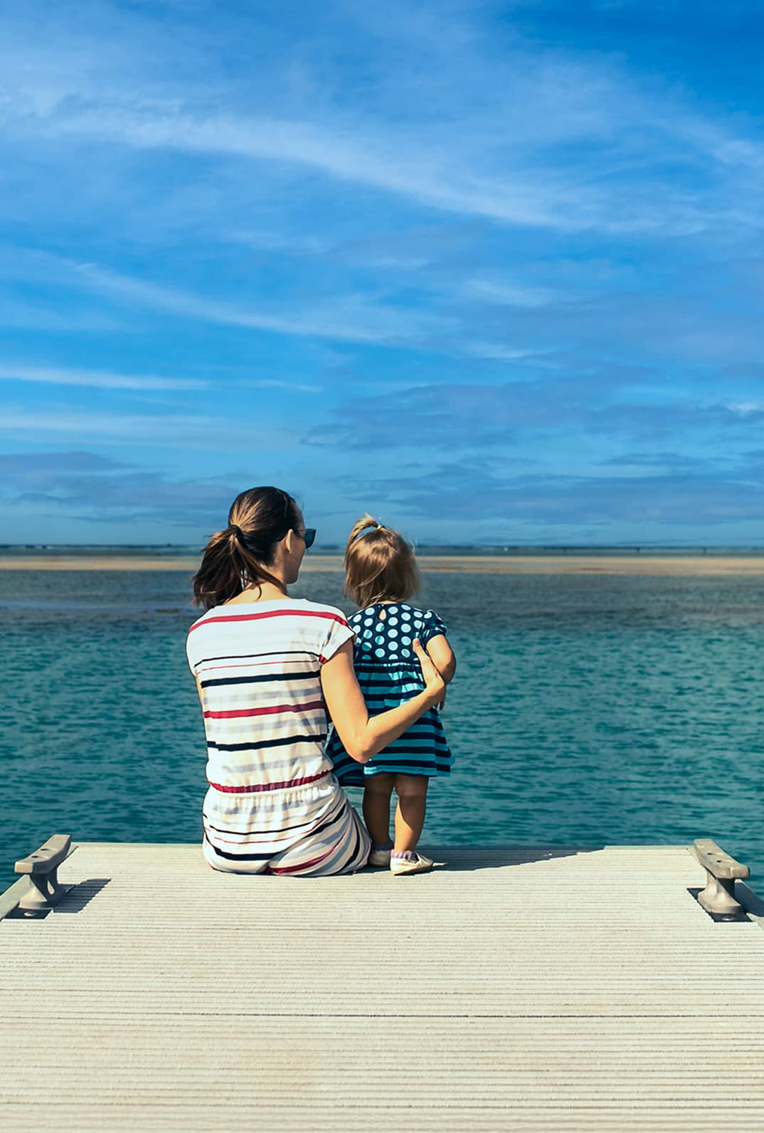 Woman holding baby on a dock looking out at the sea