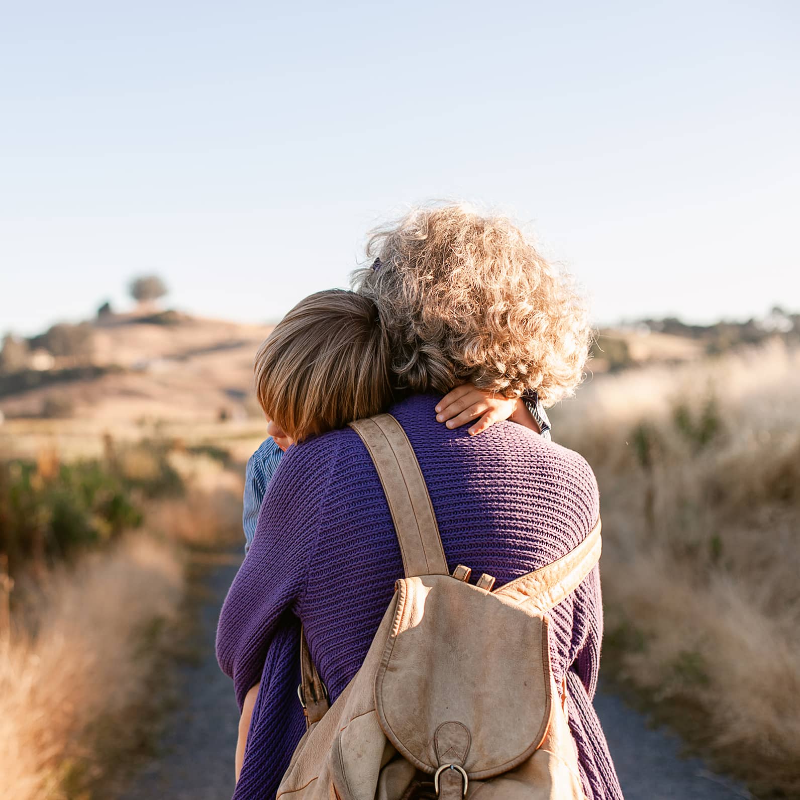 Image of woman holding young boy while walking on an asphalt road in the open meadow