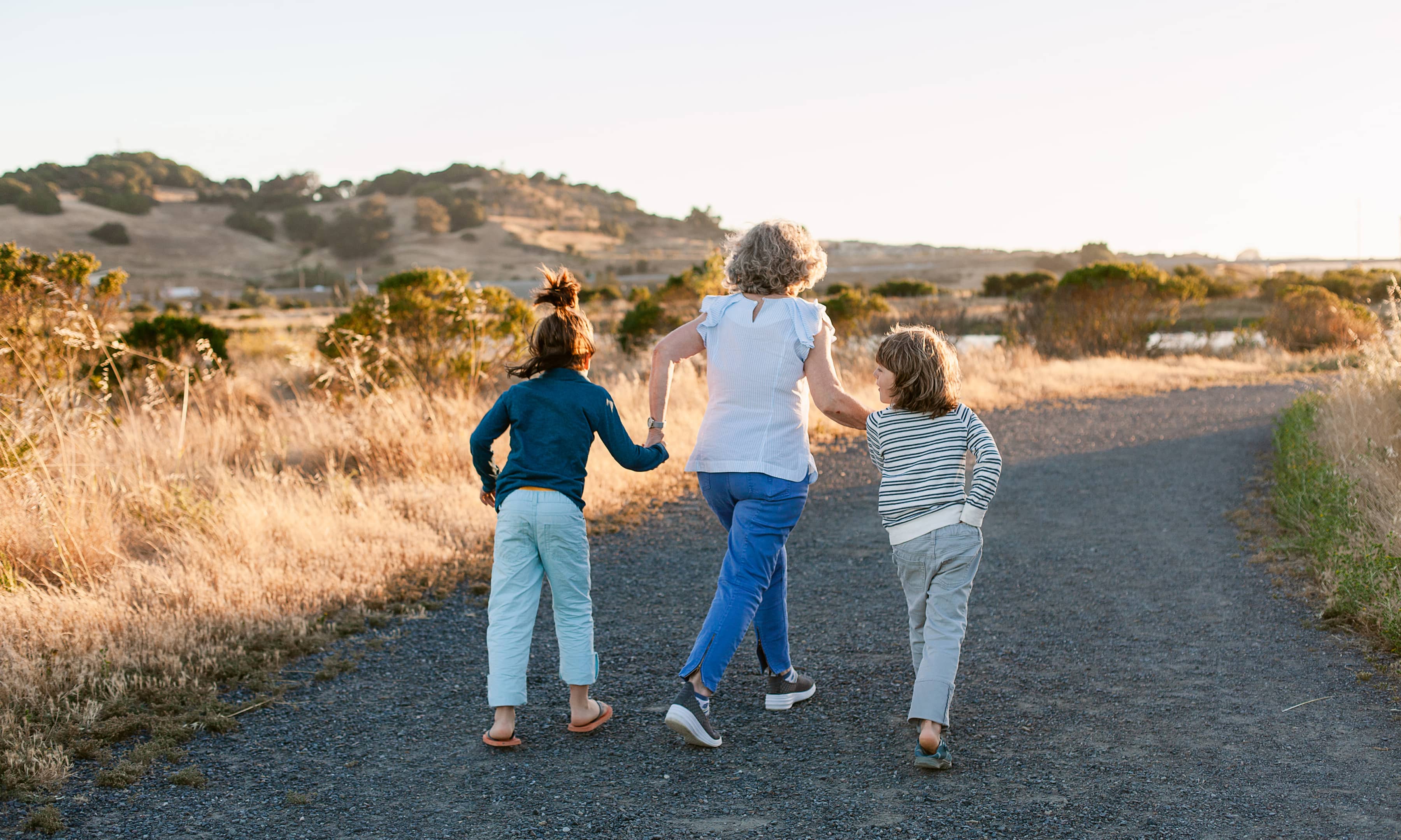 Image of a woman holding two girls hands walking up a curved road