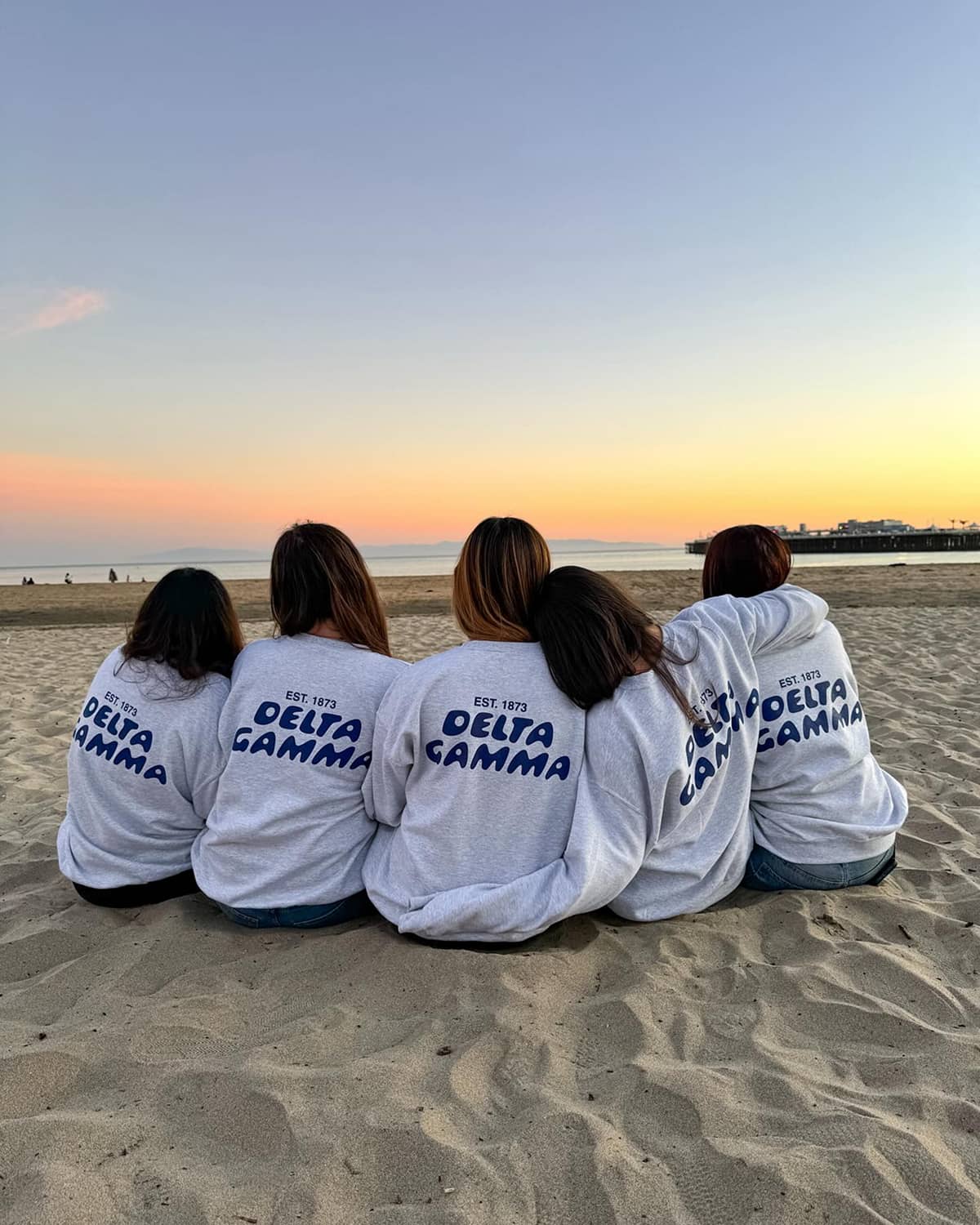 5 Delta Gamma Members sitting on the beach wearing DG long sleeve shirts
