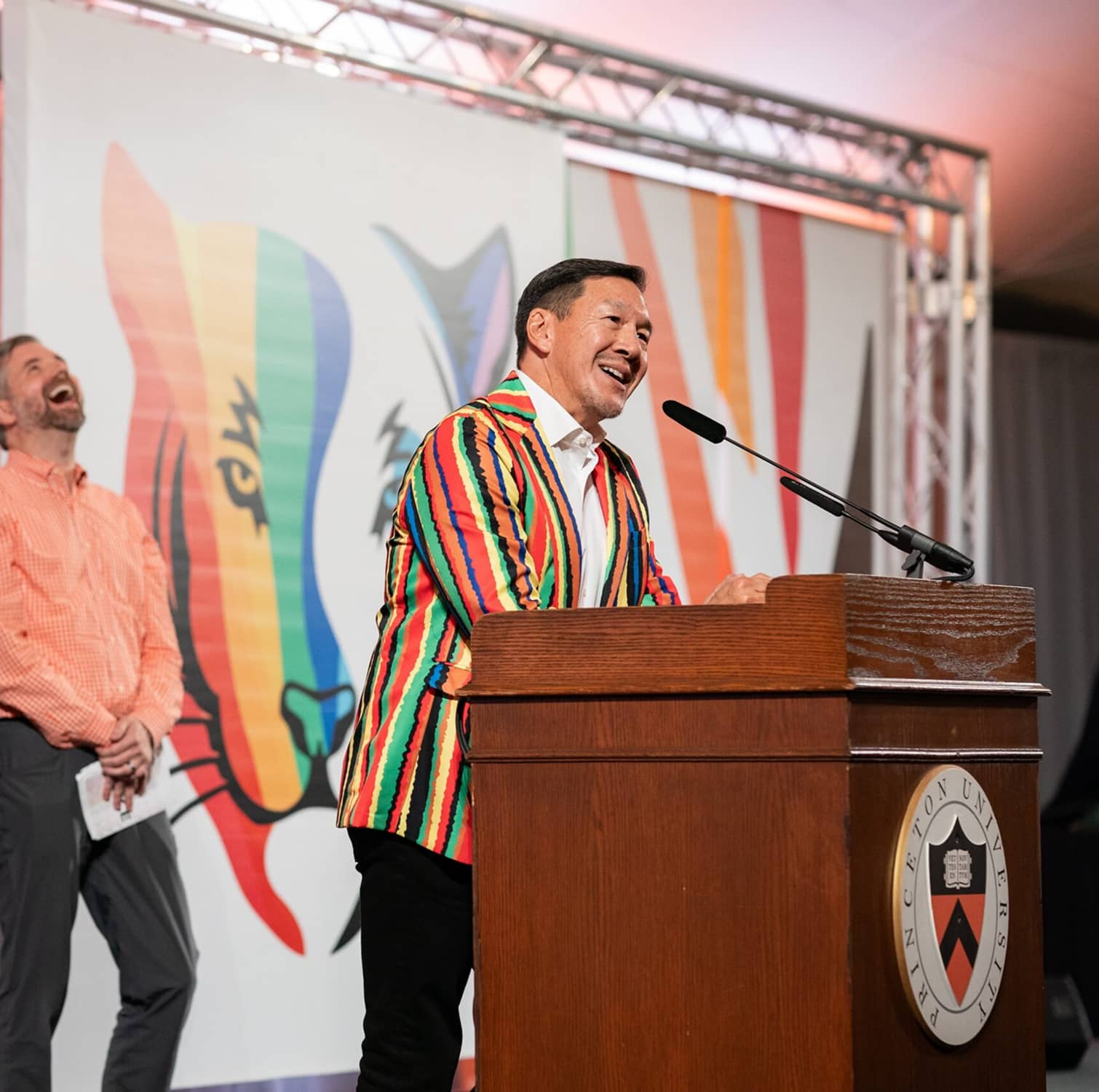 PUA Every Voice client image of speaker talking at podium wearing colorful stripped blazer