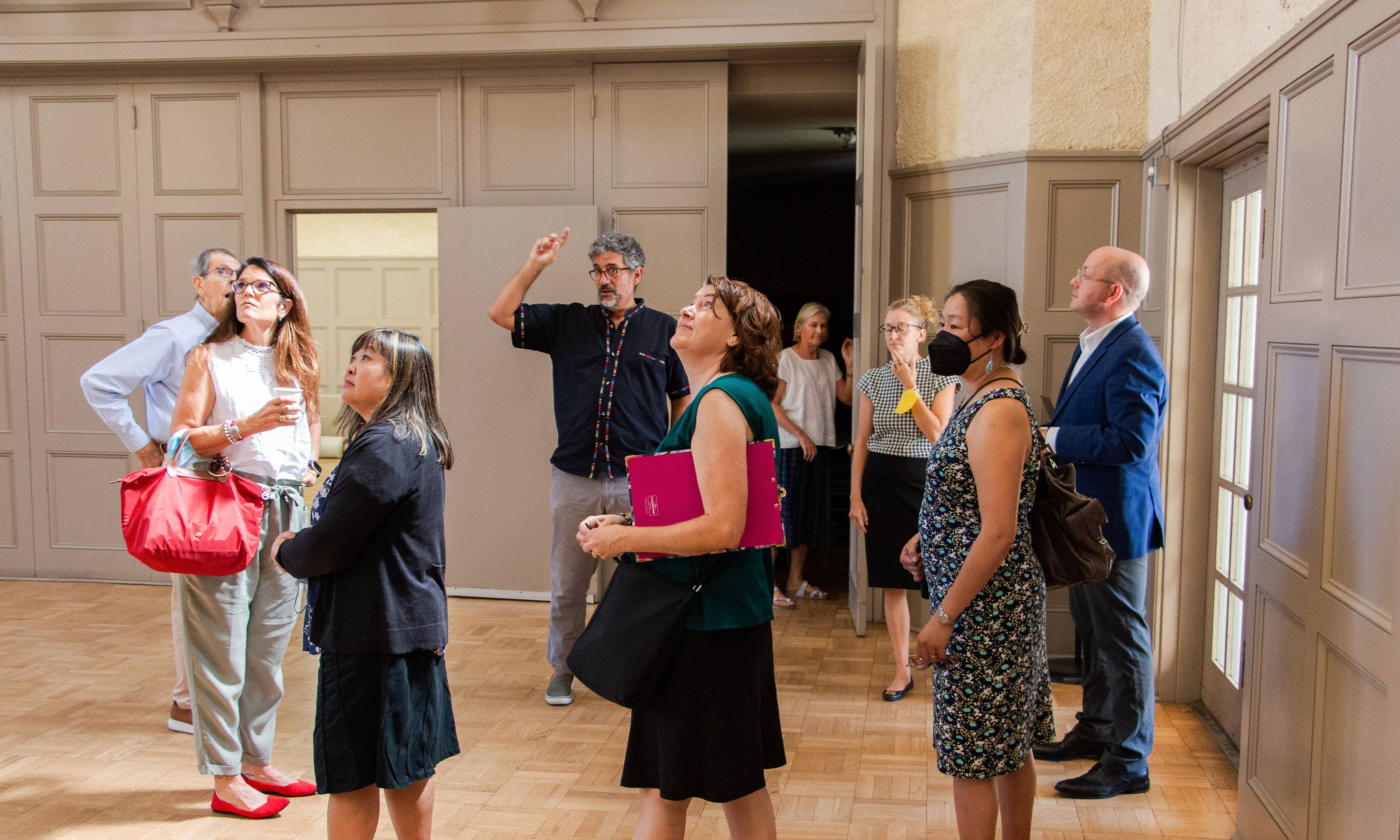 Group of people standing inside a large ballroom looking up at the ceiling.