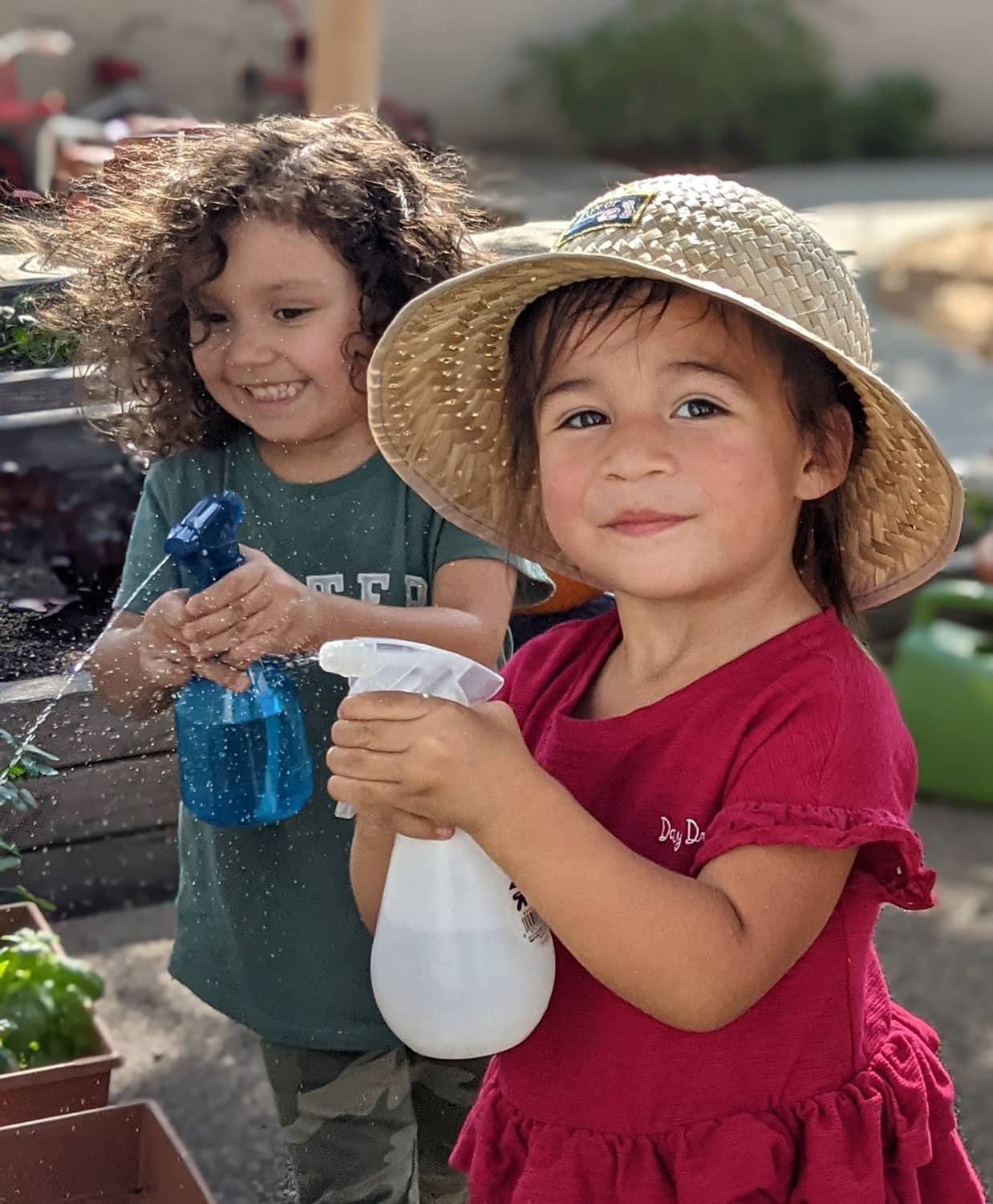 Two little girls in a garden smiling. Using spray bottles to water plants