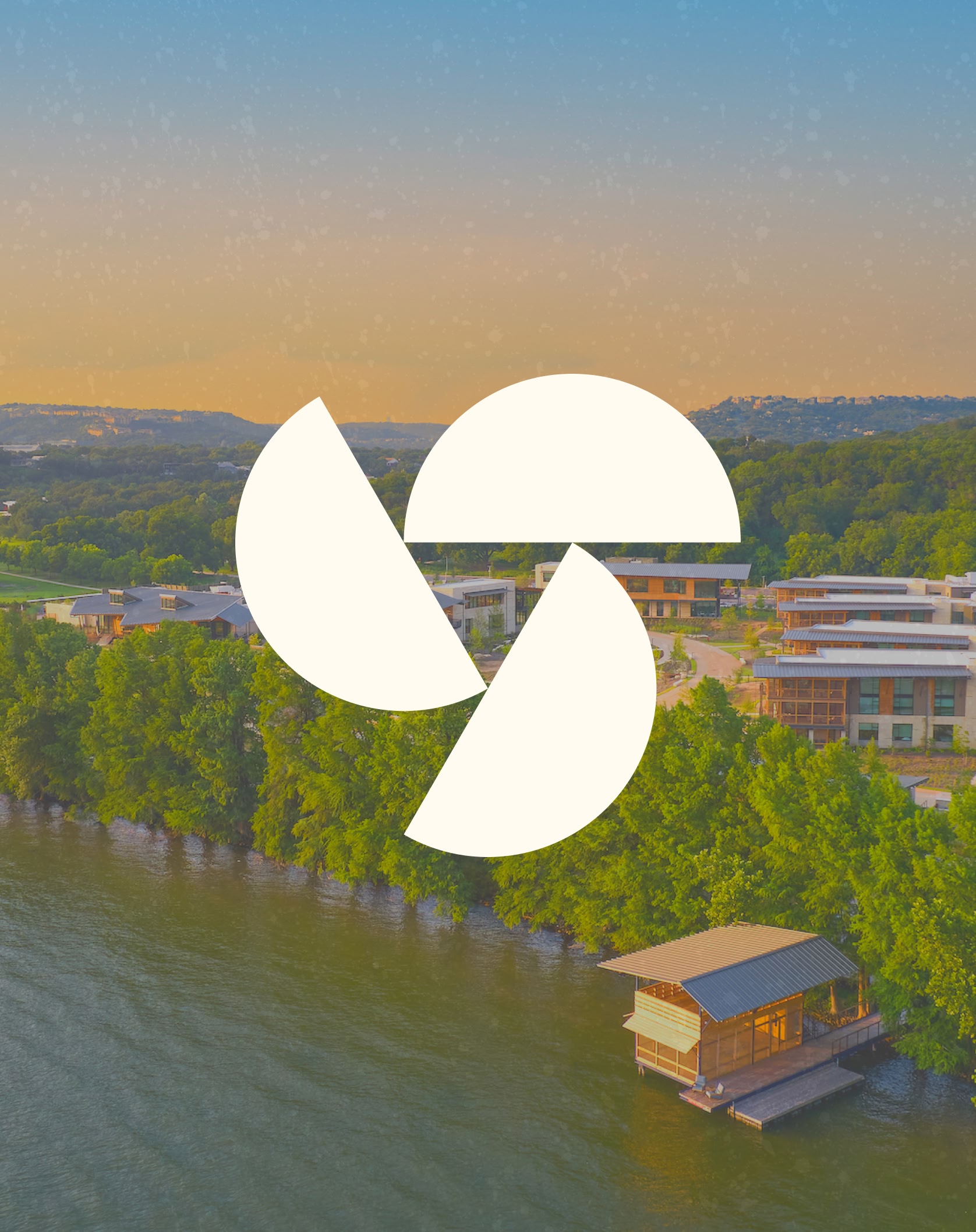 Aerial view of a lakeside campus at sunset with lush greenery and buildings. A large spiral logo is overlaid in the center, creating a serene atmosphere.