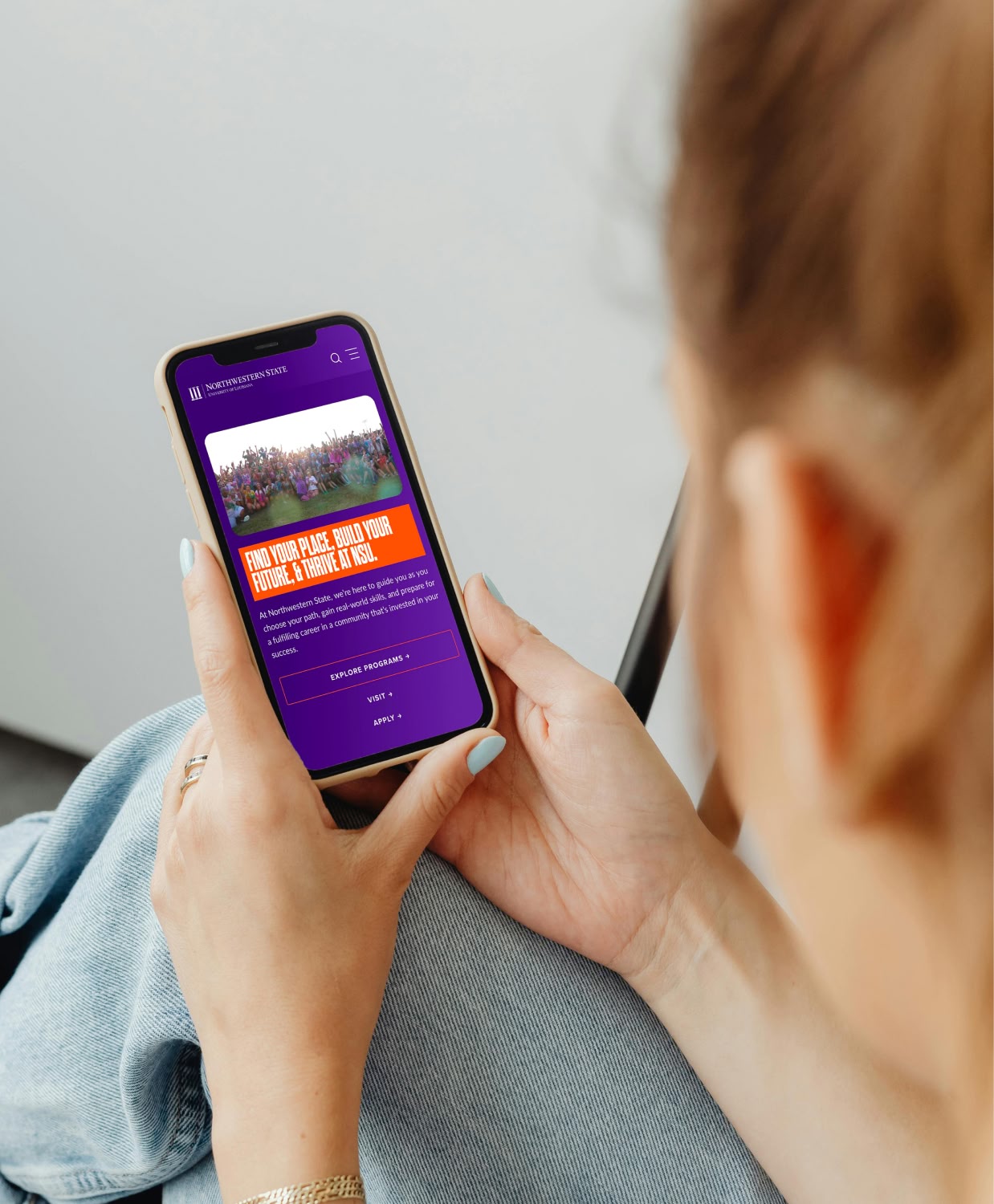 A person holds a smartphone displaying a colorful university website. The screen features a vibrant group photo and text about building a future at the school.