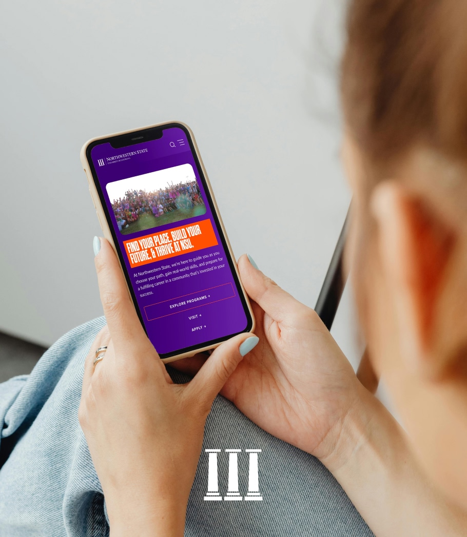 A person holds a smartphone displaying a colorful university website. The screen features a vibrant group photo and text about building a future at the school.