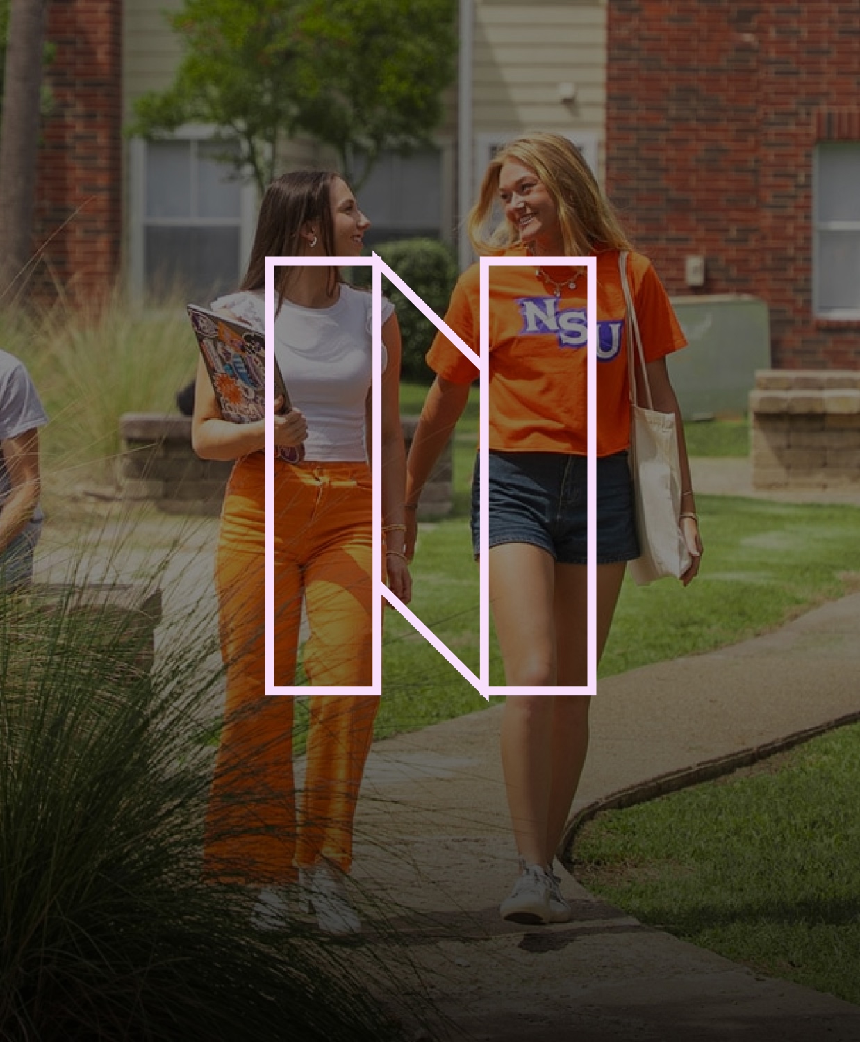 Two students walking on campus, smiling. One wears bright orange pants, the other a t-shirt reading 