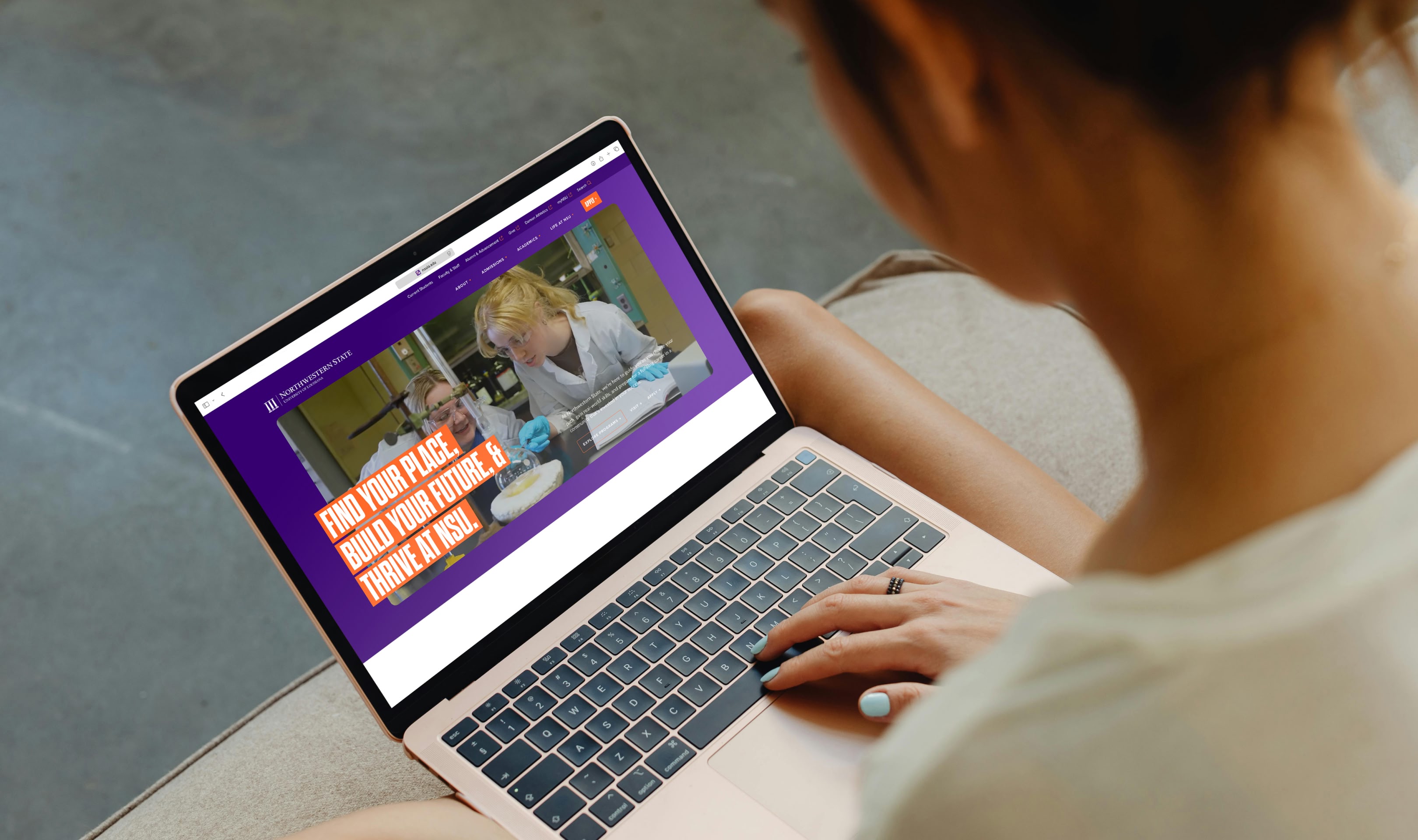 A person using a laptop displaying a university website featuring an image of a scientist in a lab and text: 